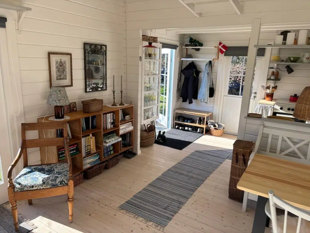 Summerhouse entrance area with coat hooks, shoe rack, bookcase, and vintage decorative objects in Scandinavian style